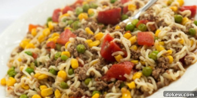 Skillet Ramen A close-up of a white plate filled with savory Skillet Ramen, showcasing ground beef, corn, green peas, and diced tomatoes mixed with ramen noodles. This colorful, easy one-pan dish is a perfect weeknight dinner solution.