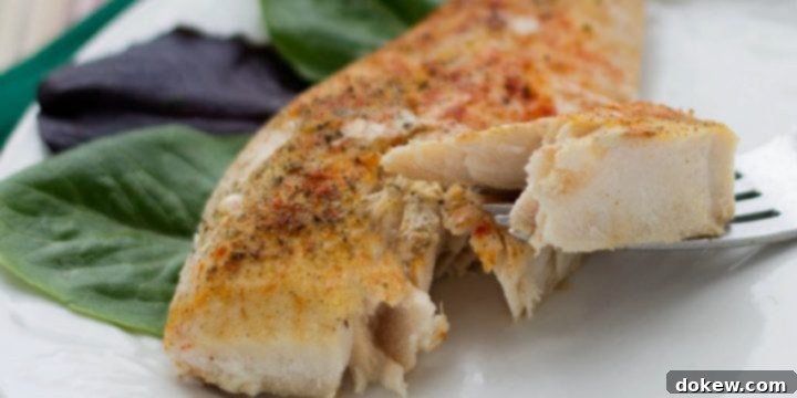 Spiced Fish Bake Seasoned fish filet on a white plate with a fork lifting one bite.
