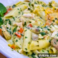 Creamy Triple Cheese Florentine Penne 2 Penne pasta with mushrooms, diced red bell pepper, chopped spinach, and cubed chicken in a cream of chicken sauce, topped with shredded cheddar cheese and garnished with two baby spinach leaves on a white plate.