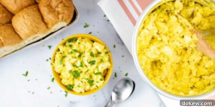Prepared egg salad garnished with chopped parsley in a white bowl with a yellow rim with whole wheat rolls in the background