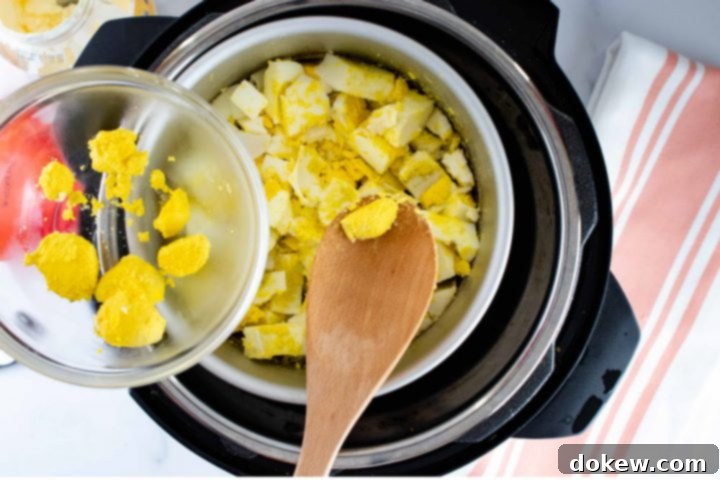 instant-pot-no-peel-egg-salad-ip-5-min Overhead view of a layer of cooked eggs in an inner pot in an Instant Pot cut into squares with a wooden spoon pulling out some of the cooked yolk