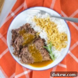 Simple Slow Cooker Pot Roast with Gravy 2 A white plate half full of roast beef and half full of rice. Roast beef and rice are both covered with gravy. There is a fork on the plate next to the rice. The plate is on an orange napkin with white stripes.