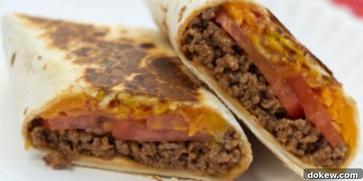 Toasted Cheeseburger Burritos A burrito with ground beef, tomato slices, and melted cheese, cut in half on a white plate.