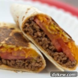 Golden Crunch Cheeseburger Burritos 2 A burrito with ground beef, tomato slices, and melted cheese, cut in half on a white plate.