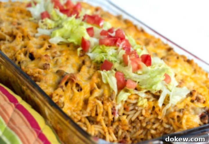 Baked Southwestern Spaghetti Clear casserole dish with spaghetti noodles, seasoned ground beef, melted cheese, topped with fresh shredded lettuce and diced tomatoes, highlighting a Tex-Mex twist on a classic baked spaghetti.