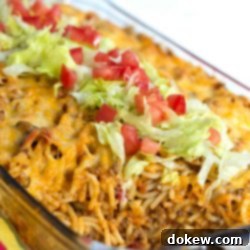 Fiesta Baked Spaghetti 2 Clear casserole dish with spaghetti noodles, ground beef, and melted cheese, topped with shredded lettuce and diced tomatoes. A perfect Baked Southwestern Spaghetti for dinner.