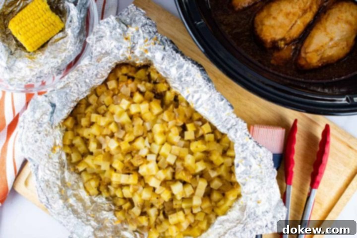 Unwrapping Cooked Dinner Components A tantalizing spread of the finished Crockpot BBQ Chicken Dinner, with an open foil packet revealing tender diced potatoes and a small corn cob peeking from its foil wrapper. In the background, the slow cooker holds the perfectly cooked chicken breasts, while a wooden cutting board with a basting brush and tongs stands ready, all inviting you to savor this delicious and easy slow cooker meal.