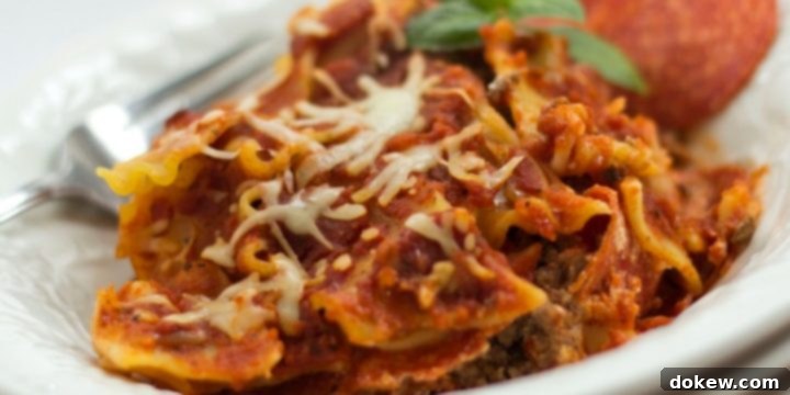 Crockpot Pizza Pasta A close-up of a white bowl filled with Crockpot Pizza Pasta, showcasing layers of ground beef, wavy lasagna noodles, melted mozzarella cheese, and slices of pepperoni on top. A fork rests on the left, ready to serve this delicious slow cooker meal.