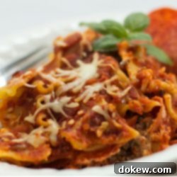 Slow Cooker Pizza Pasta Bake 2 A closer view of Crockpot Pizza Pasta in a white bowl, showing the texture of the browned ground beef, soft lasagna noodles, and rich, melted mozzarella. Pepperoni slices and a fork are visible on the side.