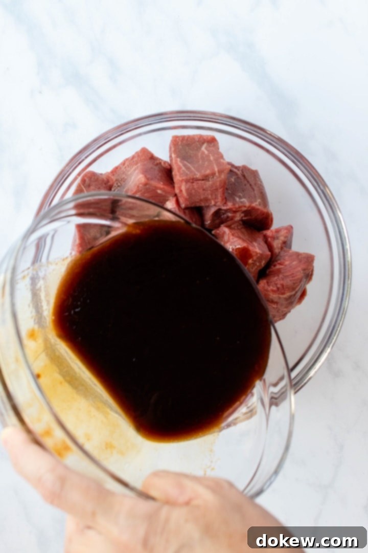soy-garlic-beef-marinade-ip-2-min Large bowl of soy garlic marinade being poured over another bowl full of cubes of beef, illustrating the marinating process