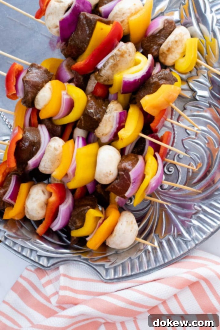 beef-vegetable-kabobs-ip-2-min uncooked kabobs of beef alternated with red, yellow, and orange bell peppers, mushrooms, and red onions on a pewter platter, ready for grilling