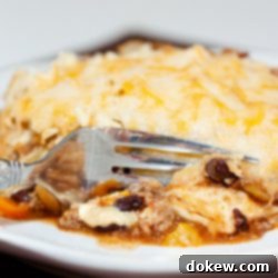 Hearty Beef & Bean Casserole 2 A tortilla covered with melted cheese, on top of ground beef, black beans, and tomatoes, all on a white plate. A fork is cutting into the tortilla.