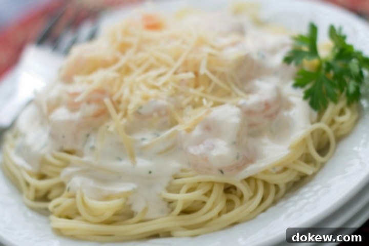 Creamy Garlic Shrimp with Angel Hair Pasta Angel hair pasta with alfredo sauce and shrimp, topped with shredded parmesan cheese, on a white plate.