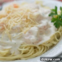 Luscious Garlic Shrimp Angel Hair 2 Angel hair pasta with alfredo sauce and shrimp, topped with shredded parmesan cheese, on a white plate.