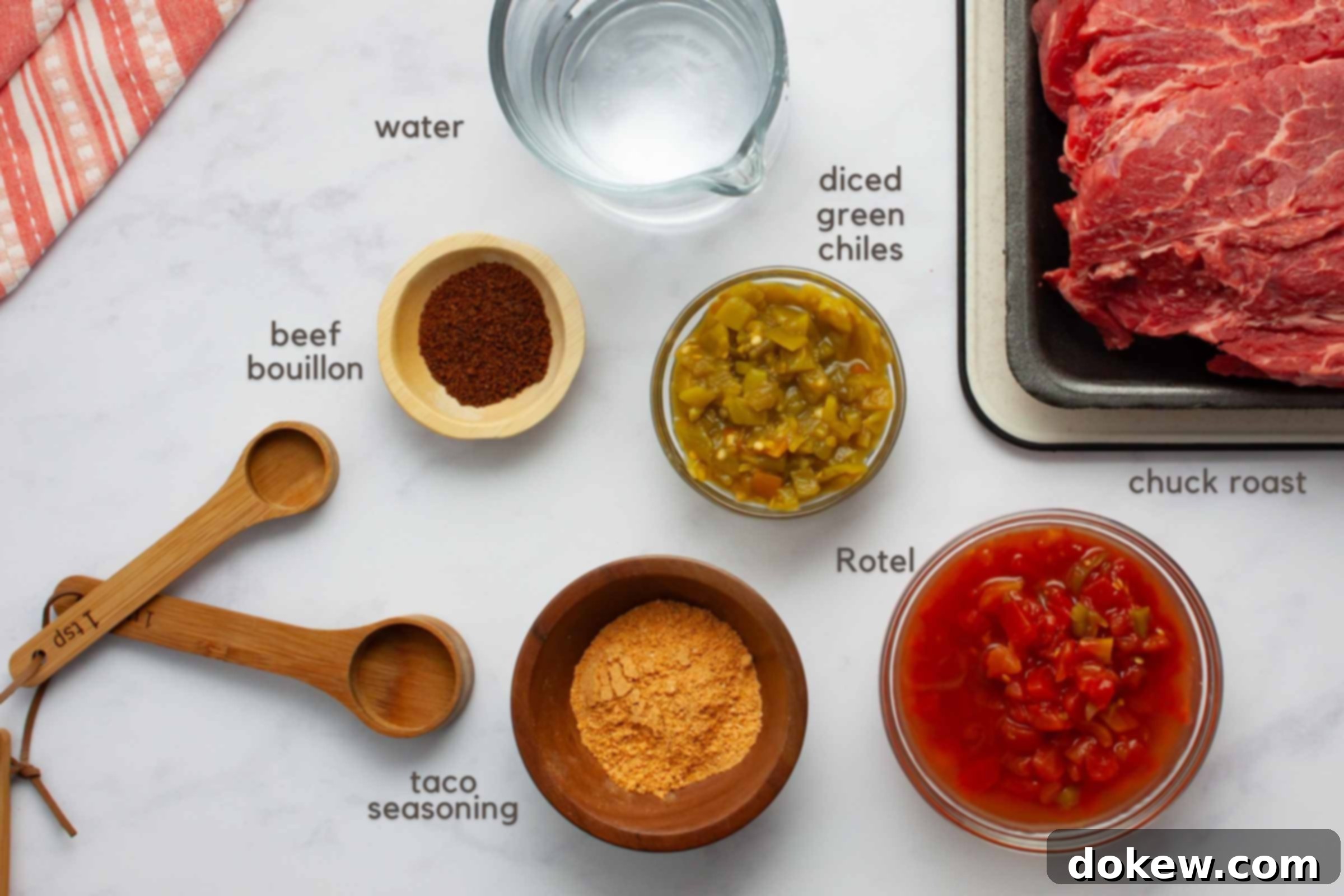 Ultimate Slow Cooker Mexican Pot Roast 2 A selection of fresh ingredients laid out on a kitchen counter, including a raw chuck roast, beef bouillon granules, a can of diced green chiles, a can of Rotel tomatoes, and a packet of taco seasoning, ready for the slow cooker.