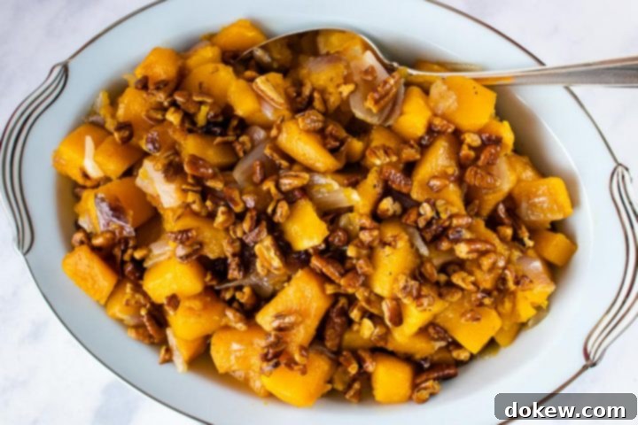 A vibrant bowl of roasted butternut squash cubes, caramelized and seasoned with nutmeg, topped generously with crunchy candied pecans, ready to be served as a festive fall side dish.