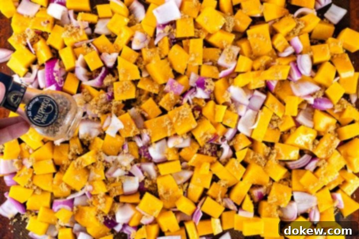 roasted-butternut-squash-candied-pecans-ip-2-min Cubed butternut squash and diced red onion spread evenly on a baking sheet, sprinkled with rich brown sugar and freshly grated nutmeg, prepared for roasting.