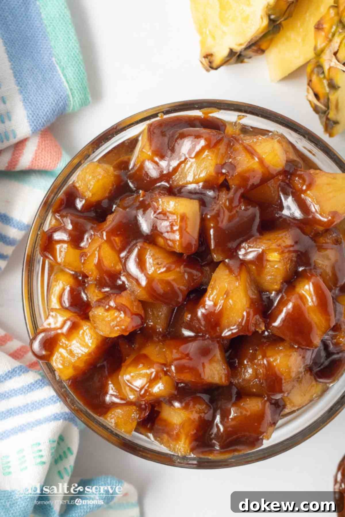 Sweet Golden Caramelized Pineapple Just 3 Ingredients 7 Bowl of caramelized pineapple chunks beside a tea towel and sliced pineapple on a counter.