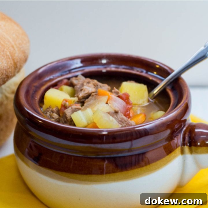 A rustic brown and white soup bowl filled with steaming Crockpot Vegetable Beef Soup, a spoon resting inside, next to a crusty loaf of fresh bread, inviting a cozy winter meal.