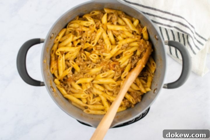 freezer-friendly-penne-pasta-bake-ip-5-min overhead view of cooked penne pasta and cooked ground beef in a creamy sauce in a large pot