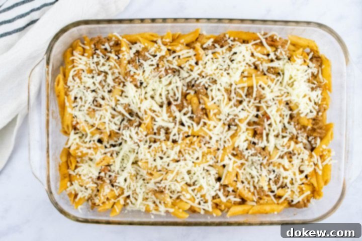 freezer-friendly-penne-pasta-bake-ip-6-min Overhead view of unbaked penne pasta bake topped with shredded cheese in a glass pan