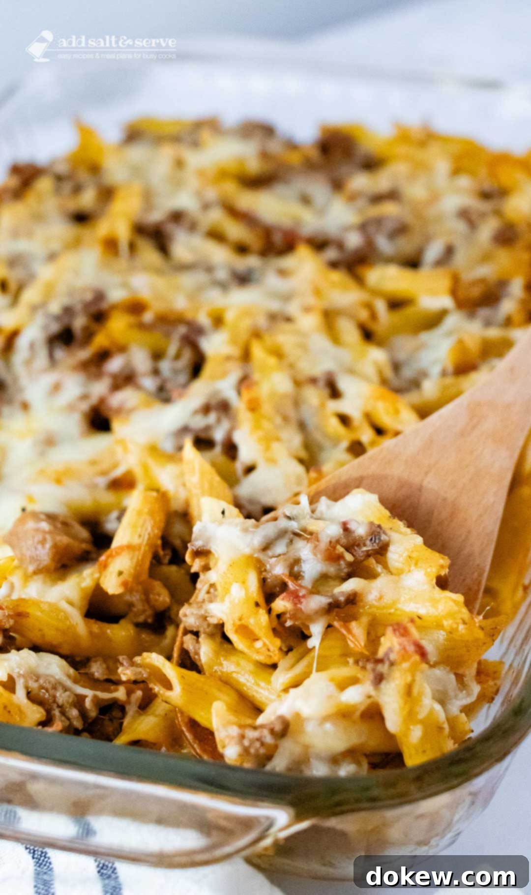 Hearty Prep-Ahead Penne Bake 3 Overhead view of penne pasta bake topped with melted cheese in a glass pan with a spoonful scooped out and held toward the camera.
