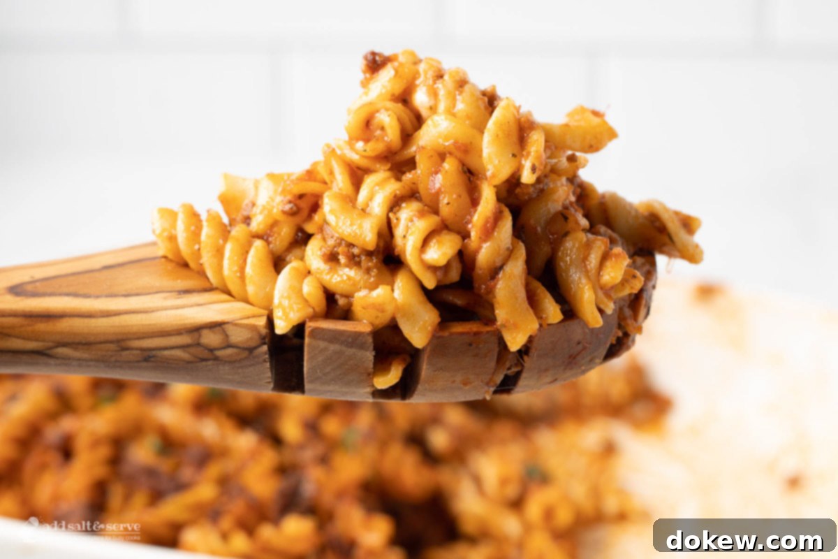 Creamy Cheesy Spirals 2 Spiral pasta bake on a wooden spoon, showcasing cheesy goodness.