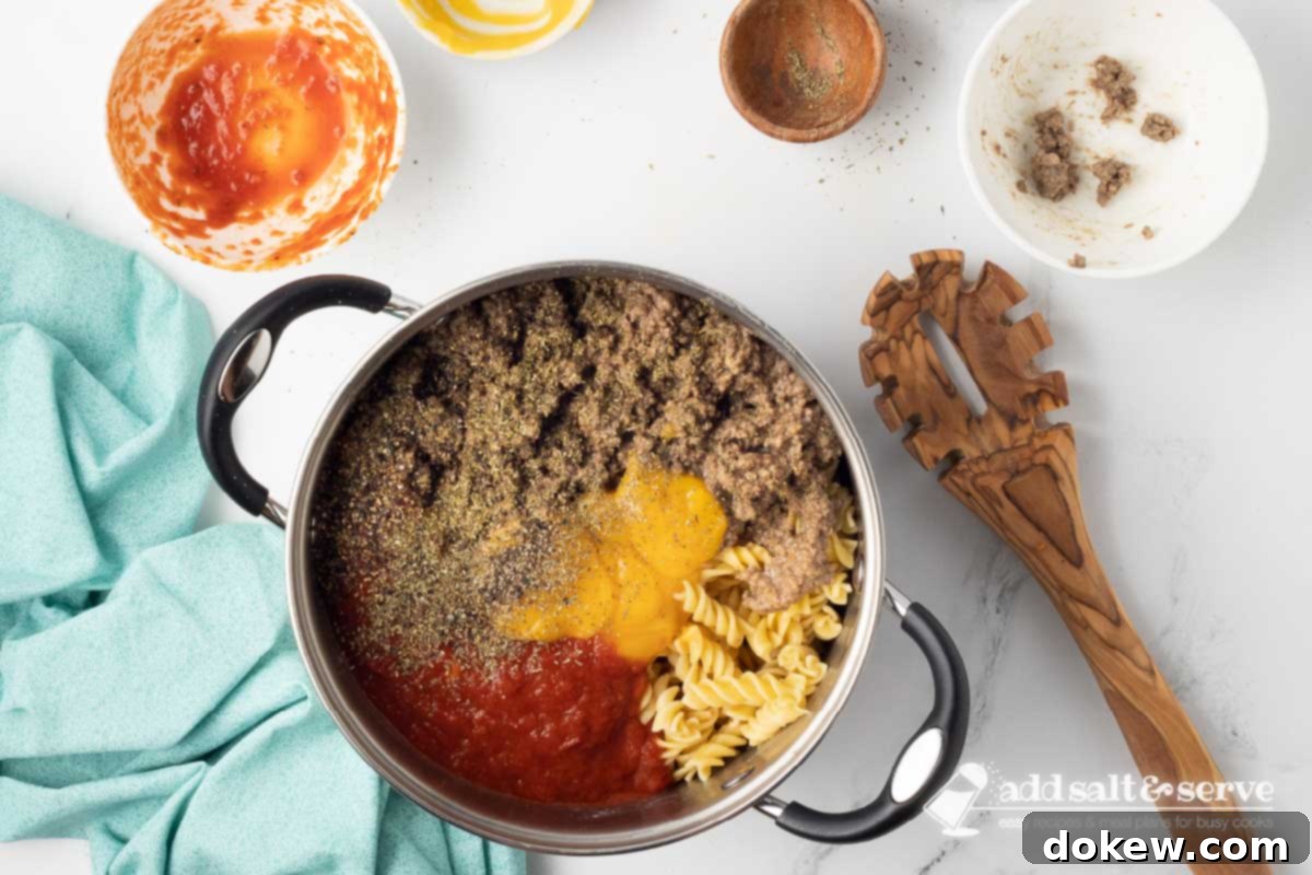 Creamy Cheesy Spirals 4 Large pot with cooked spiral pasta, cooked ground beef, marinara sauce, condensed cheddar cheese soup, Italian seasoning, and black pepper not yet mixed together.