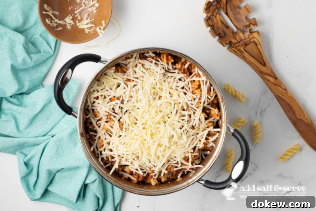 Creamy Cheesy Spirals 5 Large pot with spiral pasta recipe mixture with cheese sprinkled on top not yet mixed in.
