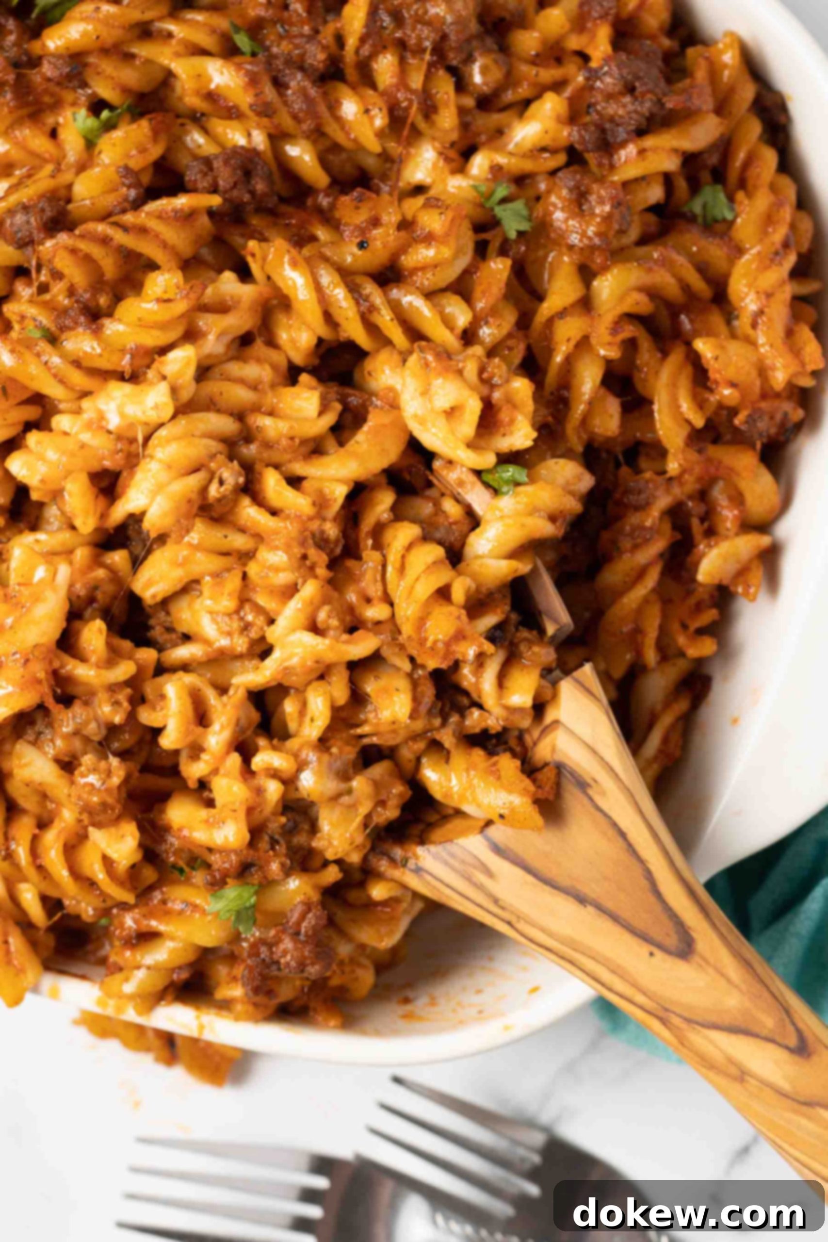 Creamy Cheesy Spirals 9 Spiral pasta bake in a white casserole dish with a serving on a wooden spoon in the dish.