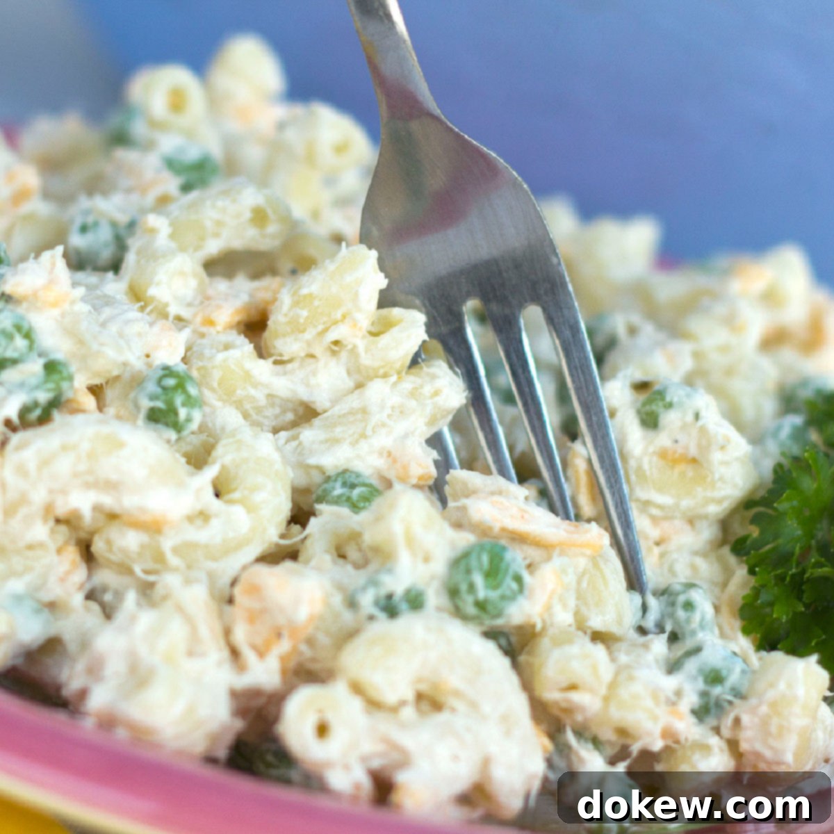 Tuna salad with pasta and peas on a red plate with a fork, garnished with parsley