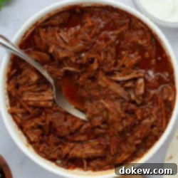 Tender Slow Cooker Beef Burritos 8 Bowl full of seasoned beef burrito filling with a fork.