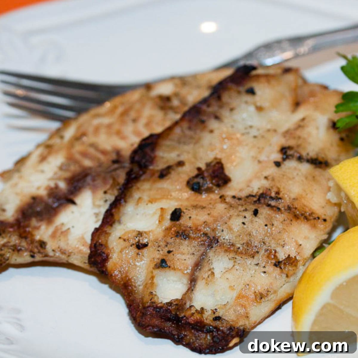 White plate with fish fillets garnished with lemon wedges and parsley