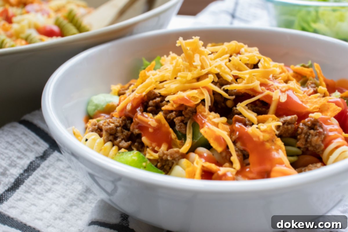 Taco Macaroni Salad 2 Bowl of seasoned ground beef, spiral pasta, lettuce, halved tomatoes, nacho cheese Doritos, and French salad dressing with shredded cheddar cheese on top.