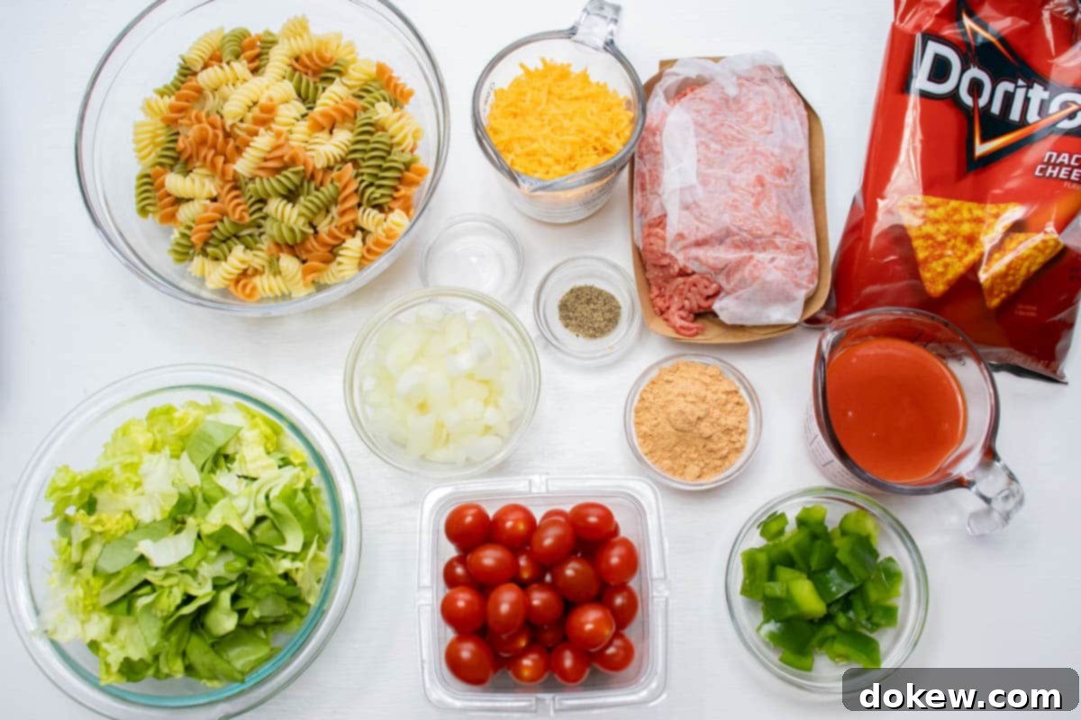 Taco Macaroni Salad 3 Overhead shot of ingredients cooked spiral pasta, lettuce, chopped onion, cherry tomatoes, chopped green bell pepper, taco seasoning mix, salt, pepper, shredded cheddar cheese, ground beef, French dressing, and nacho cheese Doritos.