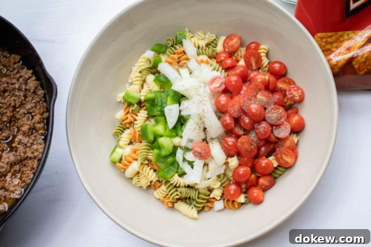 Taco Mac Salad Overhead shot of cooked spiral pasta, chopped green bell pepper, chopped onion, and halved grape tomatoes.