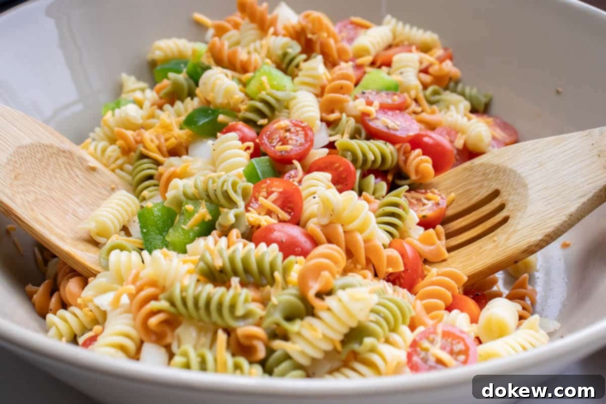 Taco Mac Salad Multi-colored rotini noodles in a bowl with chopped tomatoes and bell peppers and wooden salad spoons.