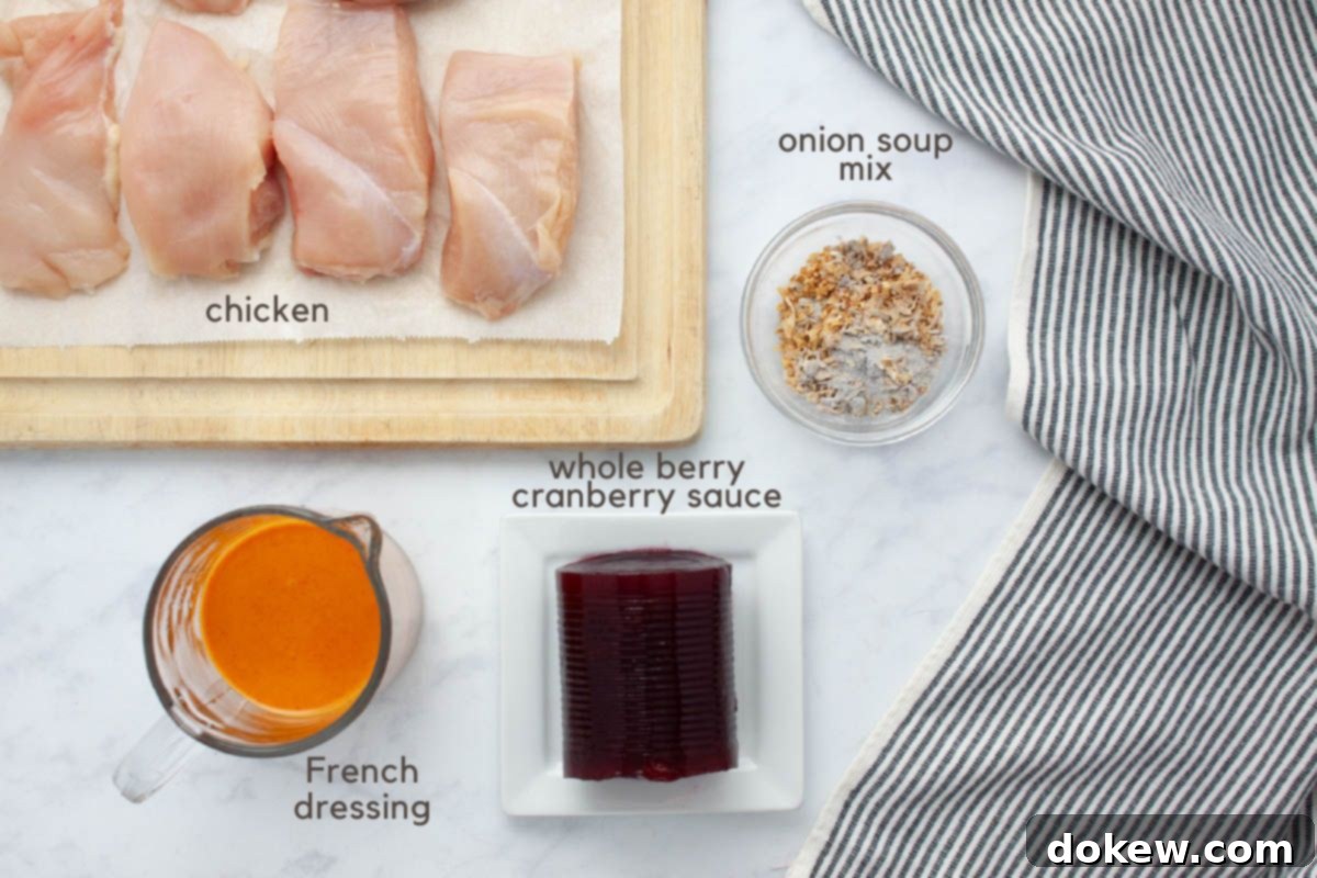 Slow Cooker Cranberry French Glazed Chicken 3 A collection of uncooked ingredients laid out on a kitchen counter, including pieces of boneless, skinless chicken breast on a cutting board, a measuring cup filled with vibrant French dressing, whole berry cranberry sauce on a small white plate, and a tiny bowl of savory onion soup mix. A grey striped tea towel is neatly folded to the side.