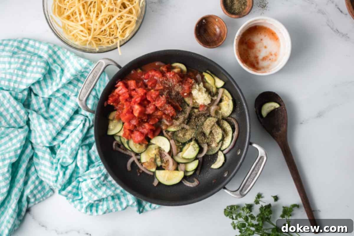 Fresh Zucchini Linguine 7 Remaining ingredients, including garlic, diced tomatoes, and Italian seasoning, added to the sautéed vegetables in a skillet.