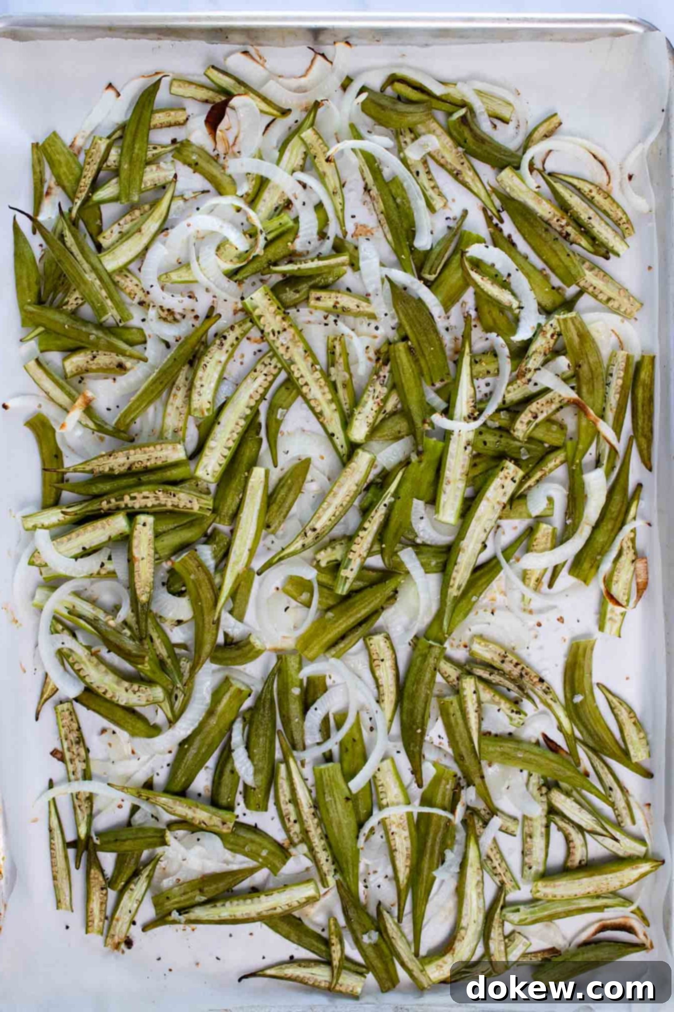 Effortless Sheet Pan Roasted Okra and Onions 4 Perfectly roasted sliced okra and onions, spread in a single layer on parchment paper on a baking sheet, showcasing their golden-brown edges and caramelized texture, ready to be removed from the oven.