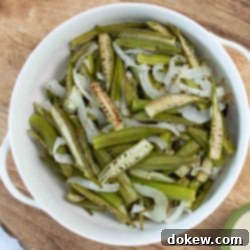 Effortless Sheet Pan Roasted Okra and Onions 6 A serving bowl filled with golden-brown roasted okra and onions, garnished with fresh herbs, showcasing a delicious and healthy side dish.