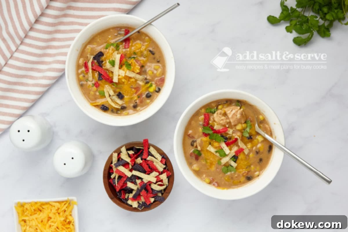 Velvety 15-Minute Chicken Enchilada Soup 2 Two bowls of creamy chicken enchilada soup, garnished generously with shredded cheddar cheese, fresh cilantro, and crispy tortilla strips. The bowls are presented on a rustic wooden surface, highlighting the vibrant colors and hearty texture of the soup.