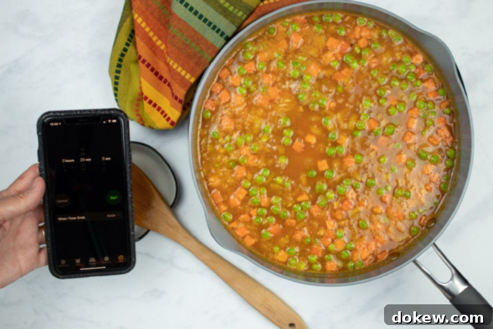 Fiesta Rice with Fresh Vegetables 7 In-process Restaurant Style Mexican Rice in a skillet, and a hand holding a phone using the timer