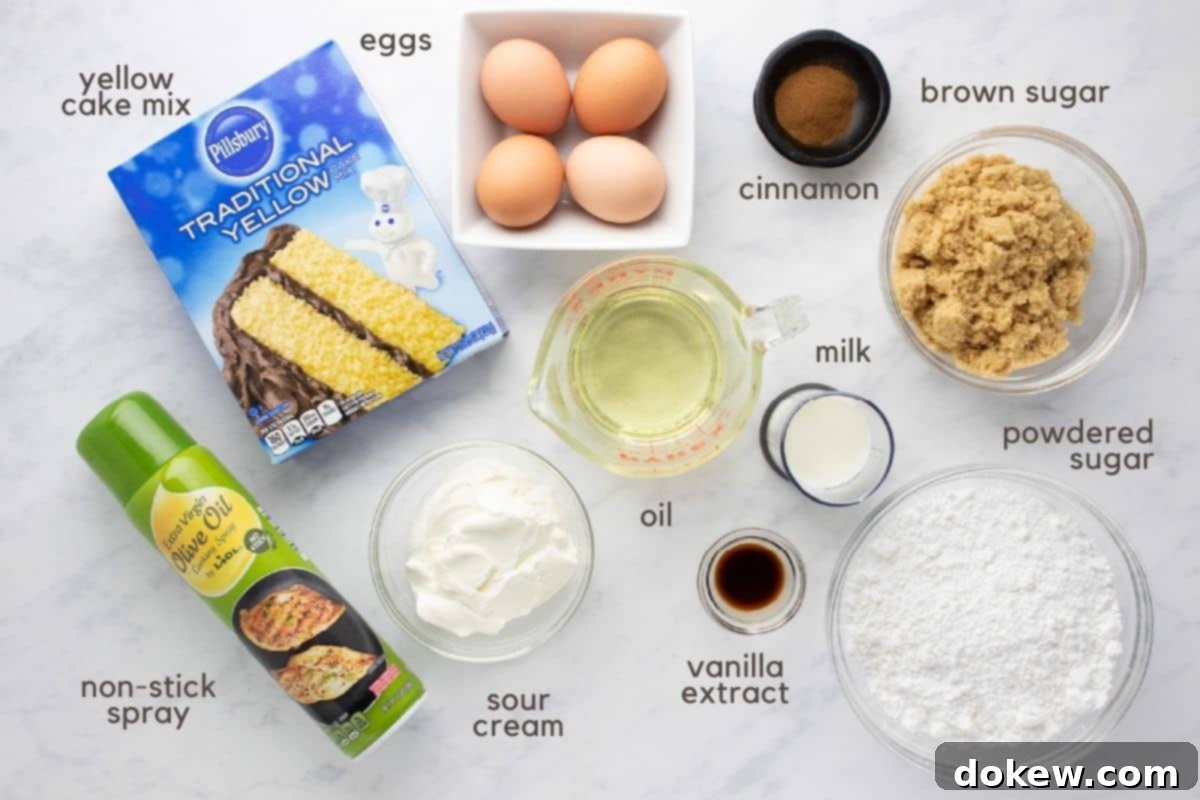 Cinnamon Honey Swirl Cake 3 All ingredients laid out for making Honey Bun Cake: a box of yellow cake mix, several eggs, a bottle of vegetable oil, a tub of sour cream, a bowl of light brown sugar, ground cinnamon, a bag of powdered sugar, a carton of milk, a bottle of vanilla extract, and a can of non-stick baking spray.