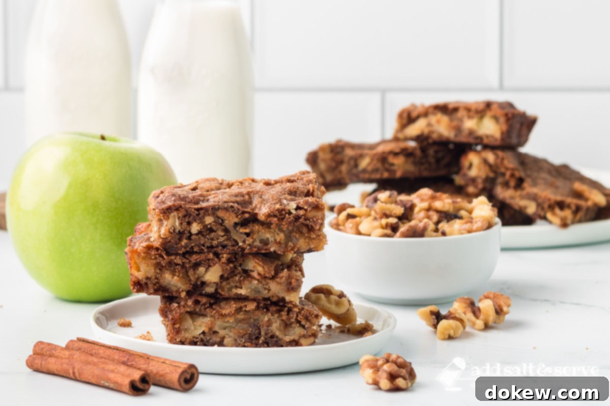 Spiced Apple Walnut Bars 2 Three Apple Walnut Bars stacked on a white plate with more bars on a plate, a bowl of walnuts, and a green apple in the background.