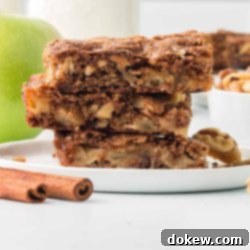 Spiced Apple Walnut Bars 12 Three Apple Walnut Bars stacked on a white plate with a bowl of walnuts and a green apple in the background.