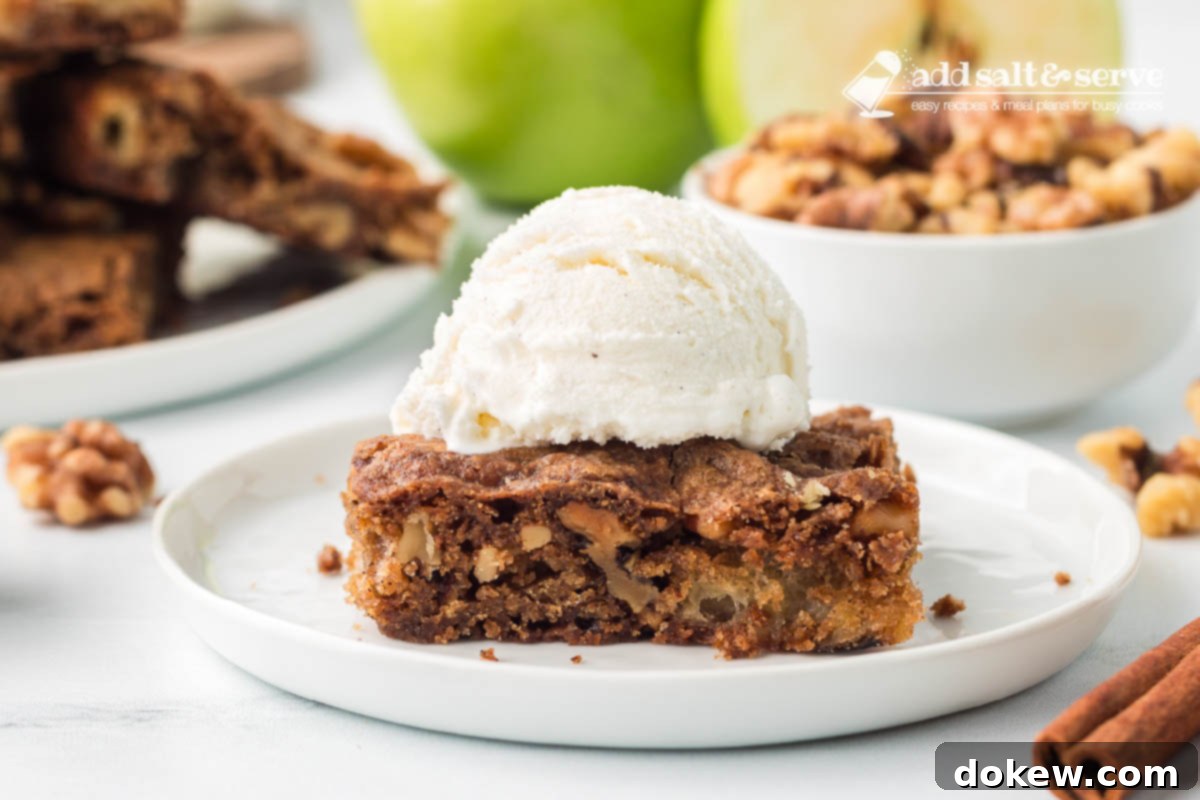 Spiced Apple Walnut Bars 10 An Apple Walnut Bar topped with vanilla ice cream on a white plate with a green apple and a bowl of walnuts in the background.