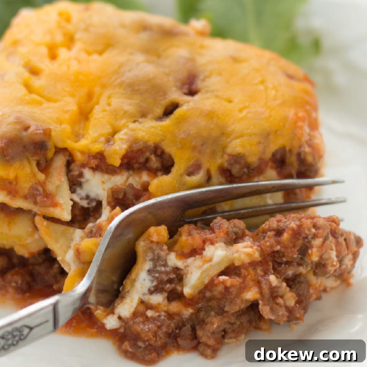 Zesty Layered Italian Beef Bake 2 A slice of Layered Italian Beef Casserole being cut by a fork, showcasing its distinct layers of meat sauce, noodles, and creamy cheese