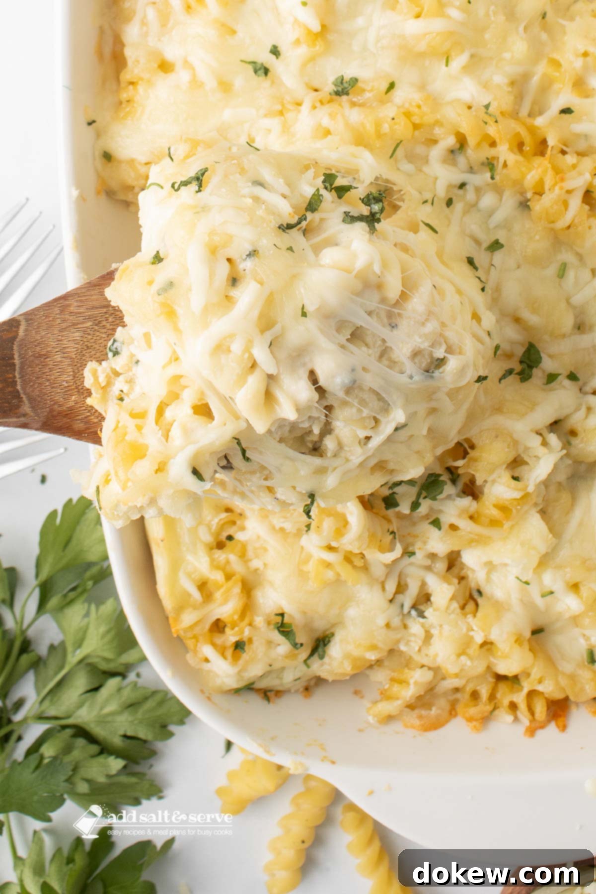 Golden Baked Alfredo Rotini 2 Rotini Pasta Bake in a baking dish with a spoonful scooped out on a wooden spoon.