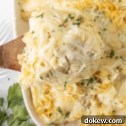 Golden Baked Alfredo Rotini 13 Rotini Pasta Bake in a baking dish with a spoonful scooped out on a wooden spoon.